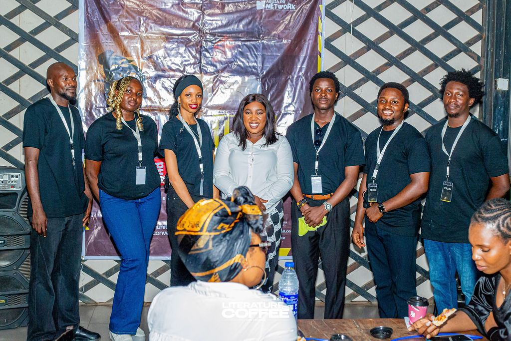 The Literature & Coffee NG crew in black T-shirts and lanyards, standing in front of the event banner.