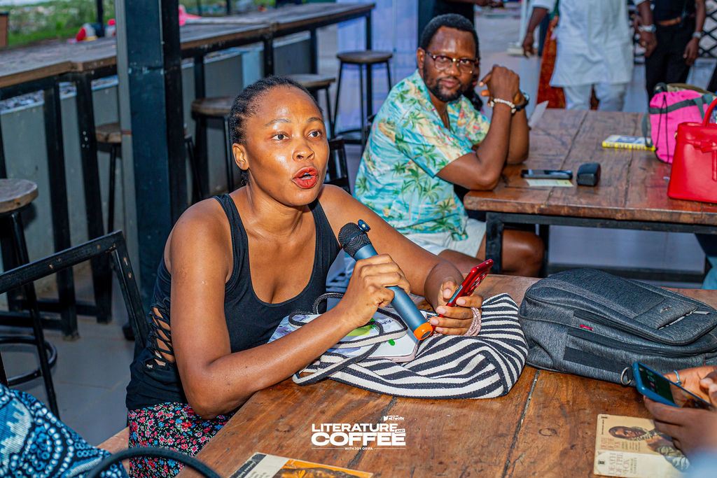 A guest speaks into a microphone at a wooden table.